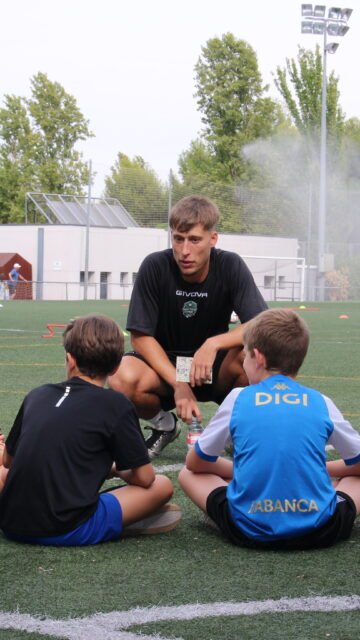 Entrenador conversando con dos niños sentados en el campo al empezar el entrenamiento en San Blas