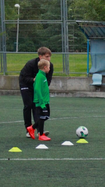 Entrenador explicando un ejercicio con conos a un niño durante la sesión de tecnificación