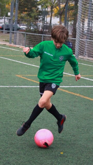 Niño con la equipación verde de High Tech Fútbol regateando con un balón rosa