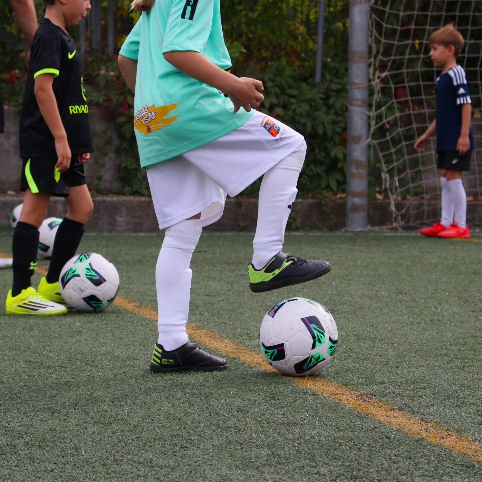 Niña con camiseta turquesa controlando el balón con la planta del pie durante un entrenamiento de tecnificación de fútbol en Madrid